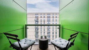 Ein Balkon mit zwei gepolsterten Stühlen, einem kleinen runden Tisch und Blick auf ein Gebäude mit vielen Fenstern.