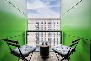 Un balcon avec deux fauteuils confortables, une petite table ronde et une vue sur un immeuble doté de nombreuses fenêtres.