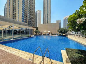 A swimming pool with a metal ladder, surrounded by lounge chairs and umbrellas, with tall buildings in the background. - WelHome - Incredible Creek Views From Th (Dubai)
