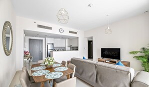 A modern living room with a sofa, dining table, and a TV. - WelHome - Incredible Creek Views From Th (Dubai)
