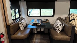 Interior compacto de una caravana, con una mesa de comedor, dos asientos acolchados y un ventanal pequeño.