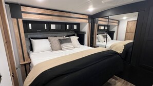 Un dormitorio moderno con una cama grande, cabecera con almacenaje integrado y un espejo en la pared.