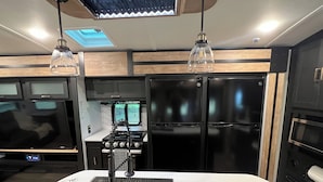 Una cocina moderna con estufa integrada, refrigerador negro y un televisor de pantalla plana grande.