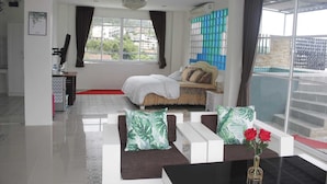 A modern hotel room with a bed, a sofa, a coffee table, and a view of the city. - Narong Ek Residence View & Pool Villa (Patong)