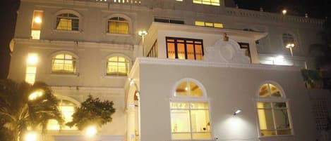 A multi-story building with illuminated windows and a car parked in front.
