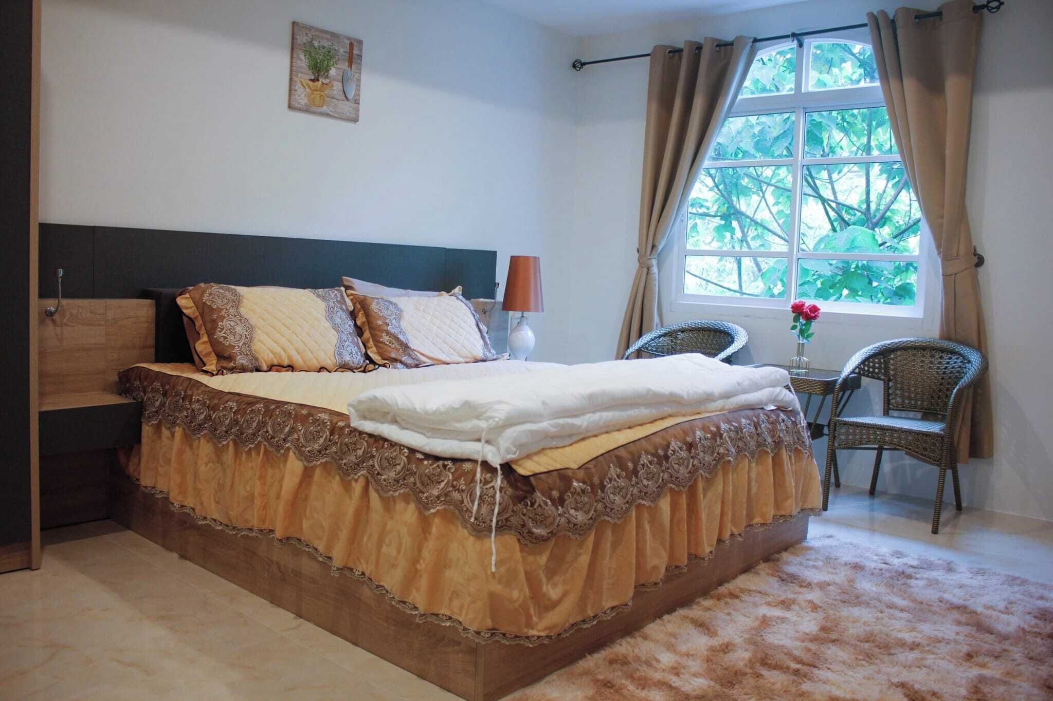A bedroom with a bed, a nightstand, a lamp, a chair, and a window with curtains.