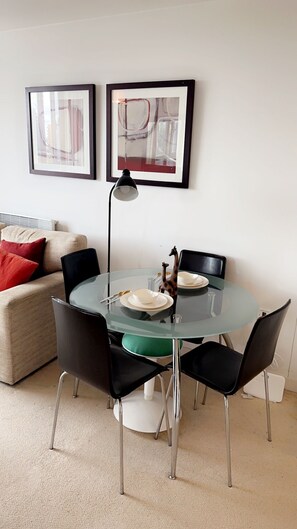 A dining area with a glass table, black chairs, and a giraffe figurine. There are framed pictures on the wall and a lamp above the table.