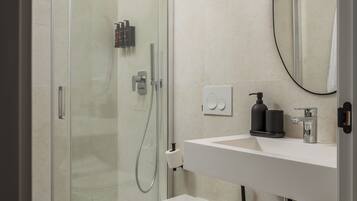 Un baño moderno con ducha acristalada, un lavabo blanco y un espejo encima.