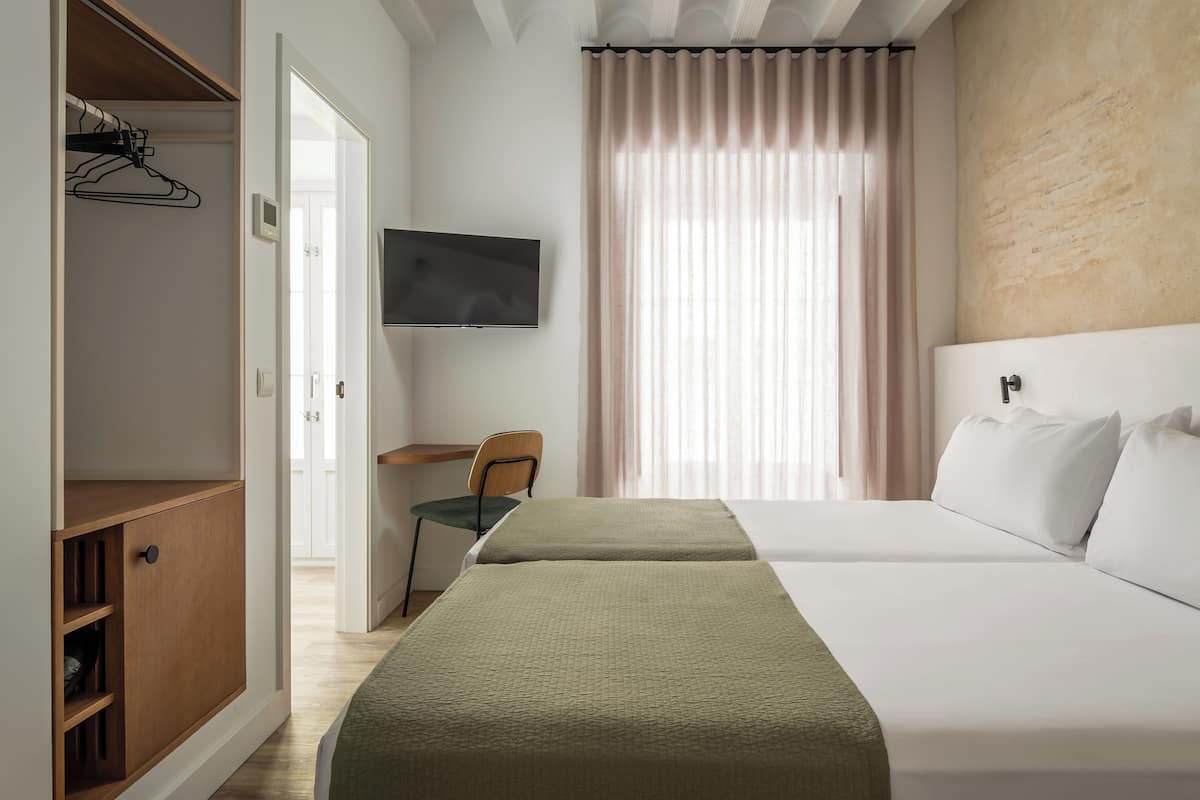 A hotel room with a bed, a desk, a chair, a TV, and a wardrobe.