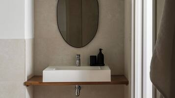 A modern bathroom with a rectangular sink, a round mirror, and a wooden shelf.