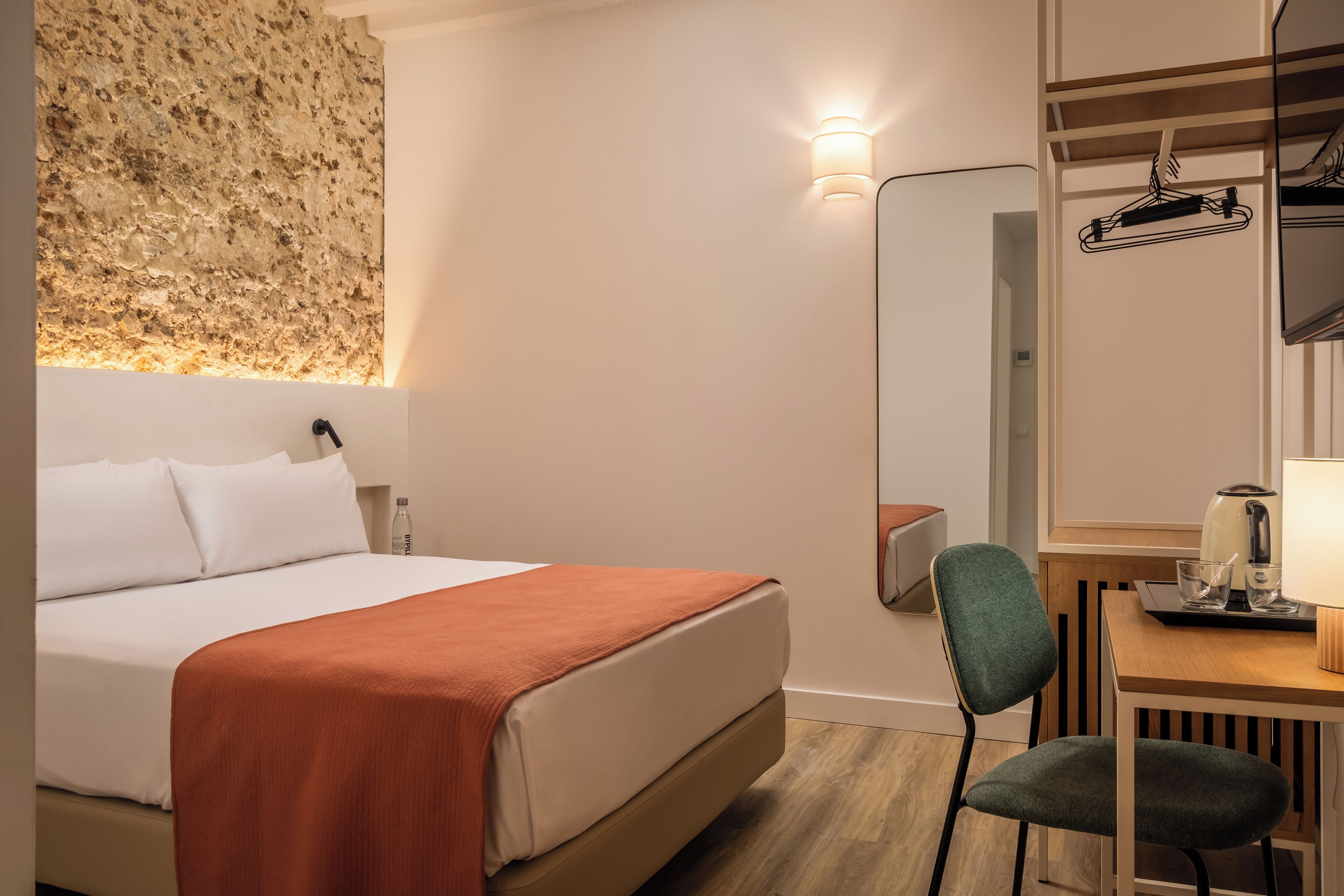 Ein Hotelzimmer mit einem Bett, einem Schreibtisch mit Stuhl, einem Spiegel und einer Wandleuchte.