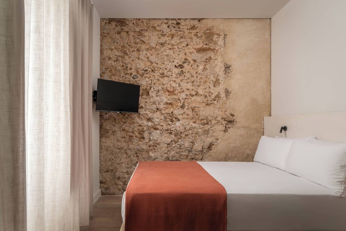 A bedroom with a stone wall, a bed with white bedding, and a mounted TV.