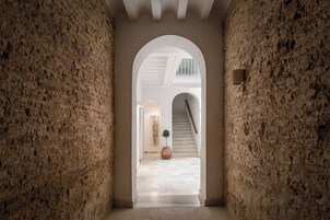 Un pasillo con pared de piedra, un arco de entrada y una escalera que sube a otro nivel.