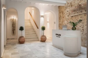 Un vestíbulo de hotel con piso de mármol, una escalera y una recepción identificada con el rótulo 'BYPILLOW Casa Grandes'.