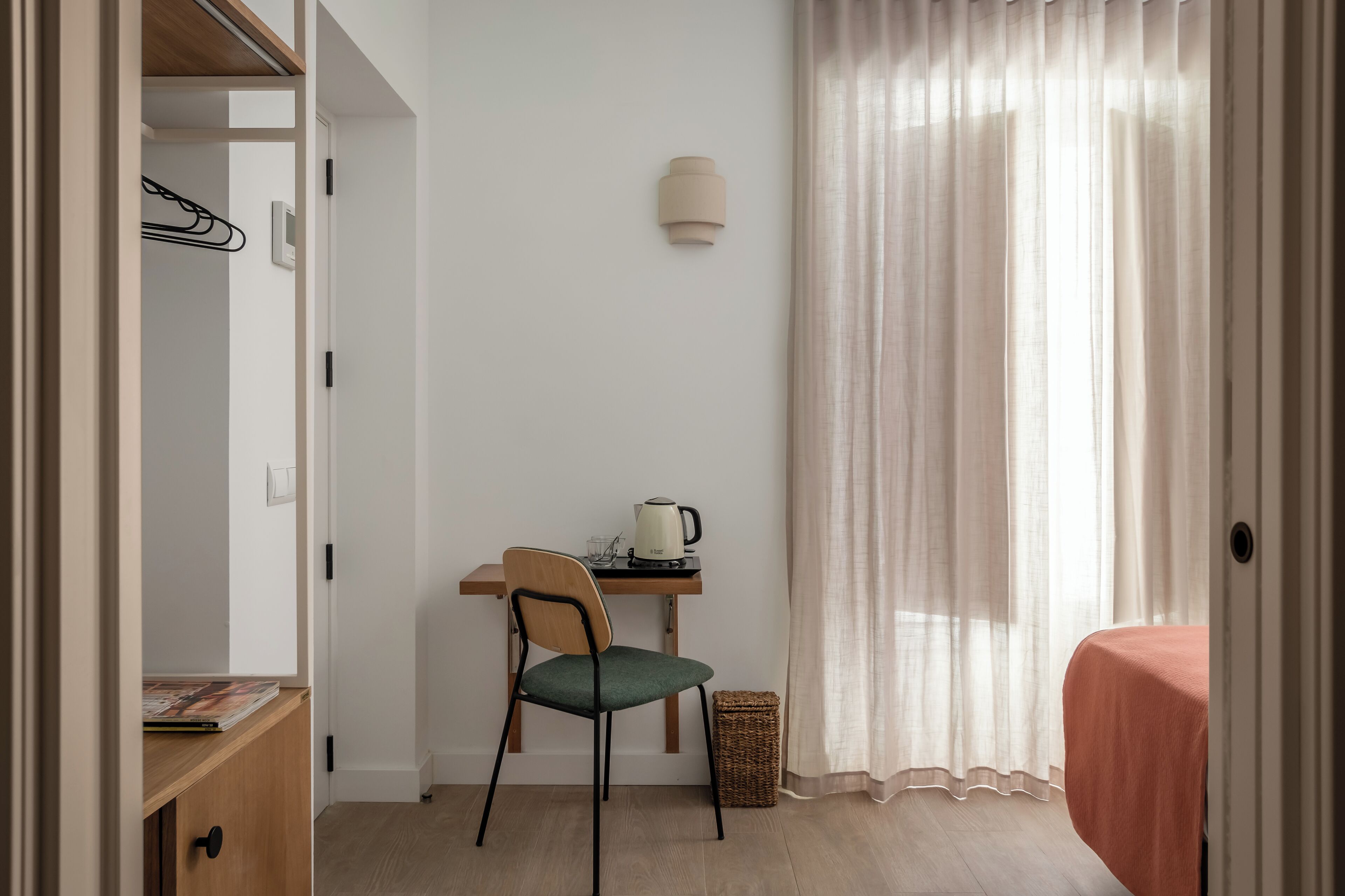 A small, neatly organized room with a desk, chair, and a bed.