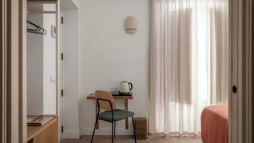 A small, neatly organized room with a desk, chair, and a bed.