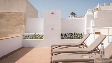 A rooftop terrace with beige lounge chairs, a water feature, and potted plants.