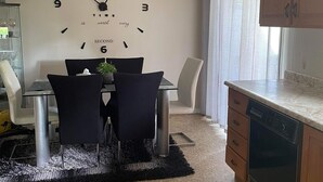 Moderni keittiö, jossa on ruokailutila. Keittiöön kuuluu kannustavaa tekstiä sisältävä kello, ruokapöytä tuoleineen, keittiösaareke ja astianpesukone.