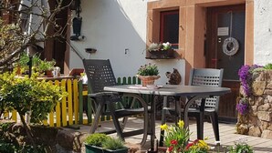 An outdoor patio with a table and chairs, surrounded by potted plants and a yellow fence.