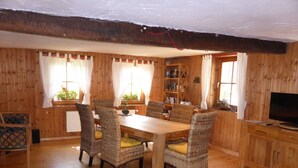 A wooden-paneled room with a dining table and chairs, a bookshelf, and a television.