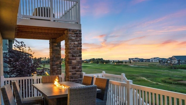Eine Terrasse mit Feuerstelle, Korbmöbeln und Blick auf einen Golfplatz bei Sonnenuntergang.
