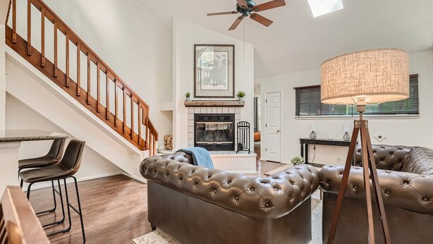 A modern living room with a brown leather sofa, a wooden staircase, a ceiling fan, and a fireplace. - New! Urban Oasis - Pool Access - Fireplace - 31 Day Rental (Aurora)