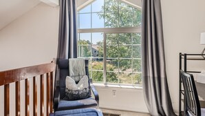 A room with a large window, a wooden railing, a blue chair with a white throw, and a black chair. - New! Urban Oasis - Pool Access - Fireplace - 31 Day Rental (Aurora)