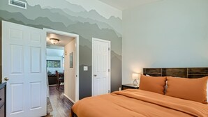 A bedroom with a large bed, two white doors, a wooden headboard, and a mountain-themed wall. - New! Urban Oasis - Pool Access - Fireplace - 31 Day Rental (Aurora)