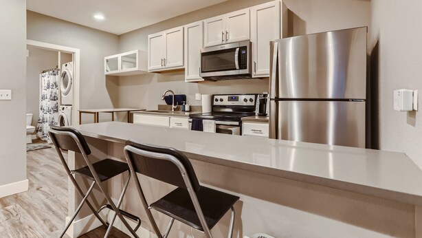 A modern kitchen with white cabinets, stainless steel appliances, and a bar area with two chairs.