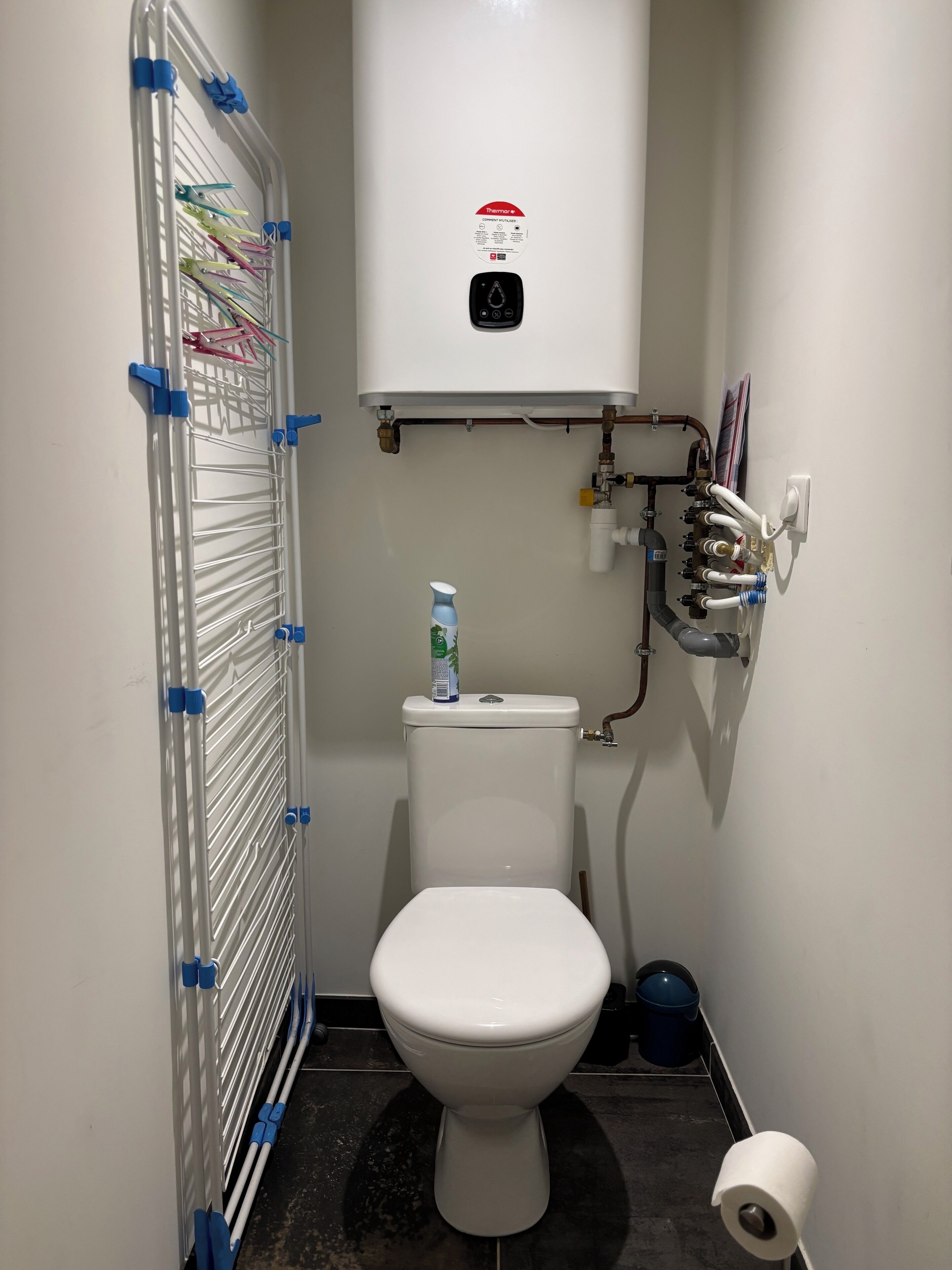 Un baño pequeño con inodoro blanco, calentador de agua y un tendedero con pinzas.