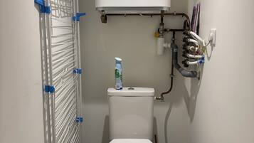 Un baño pequeño con inodoro blanco, calentador de agua y un tendedero con pinzas.