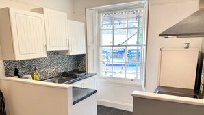 A kitchen with white cabinets, a tiled backsplash, a window with a view of a blue building, and a stainless steel range hood. - Torquay, 2 Bedrooms, Sleep 6, Free Parking, Torbay (Torquay)