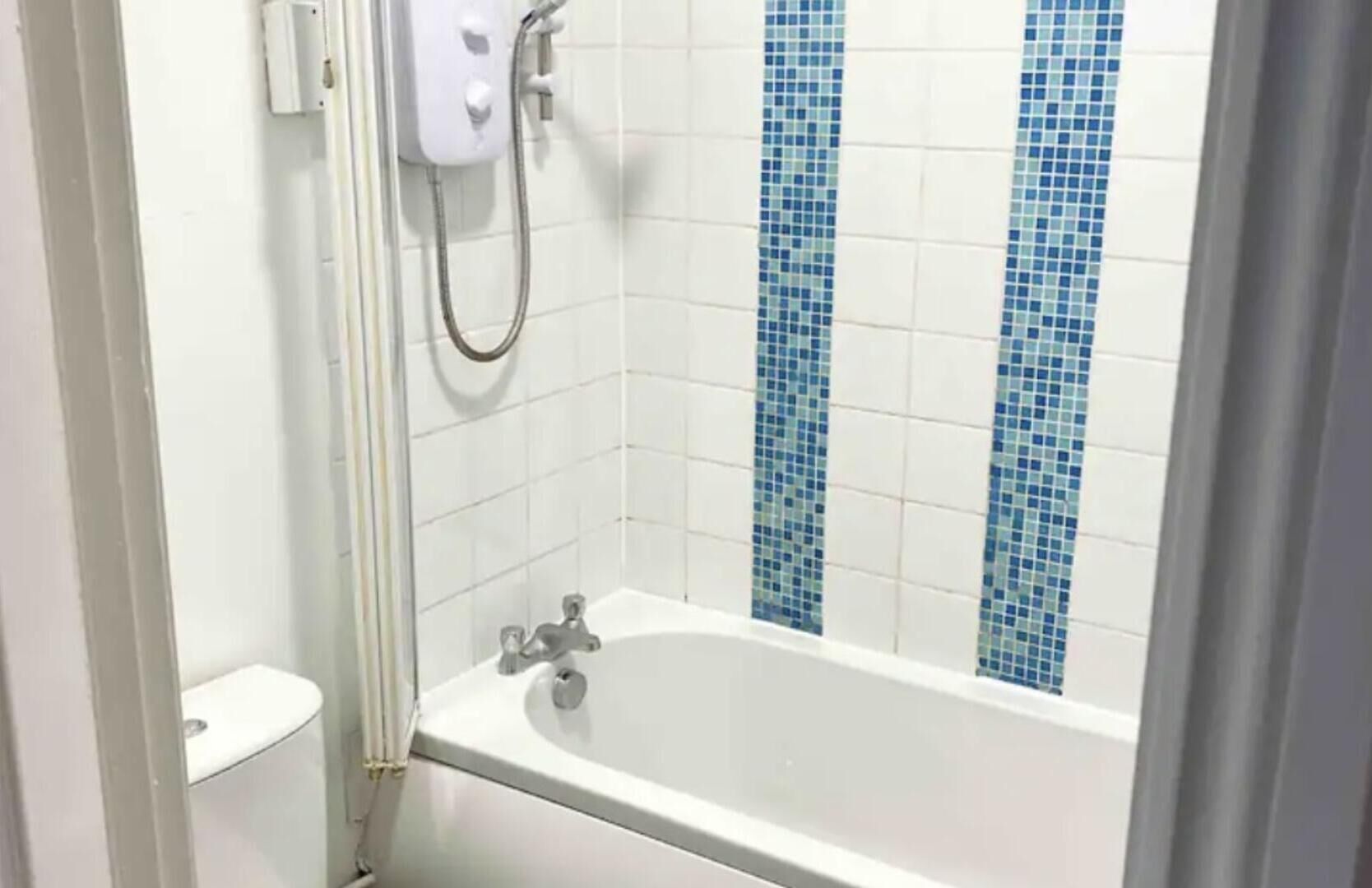 A bathroom with a white bathtub, a shower, and blue mosaic tiles on the wall.