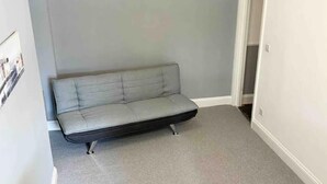 A grey sofa in a corner of a room with grey carpet and light grey walls. - Torquay, 2 Bedrooms, Sleep 6, Free Parking, Torbay (Torquay)