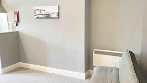 A room with a grey carpet, a grey sofa, a white radiator, and a framed picture on the wall. - Torquay, 2 Bedrooms, Sleep 6, Free Parking, Torbay (Torquay)