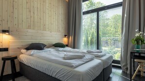 A modern bedroom with a wooden headboard, a large bed with white linens, a small stool, and a desk with a plant.