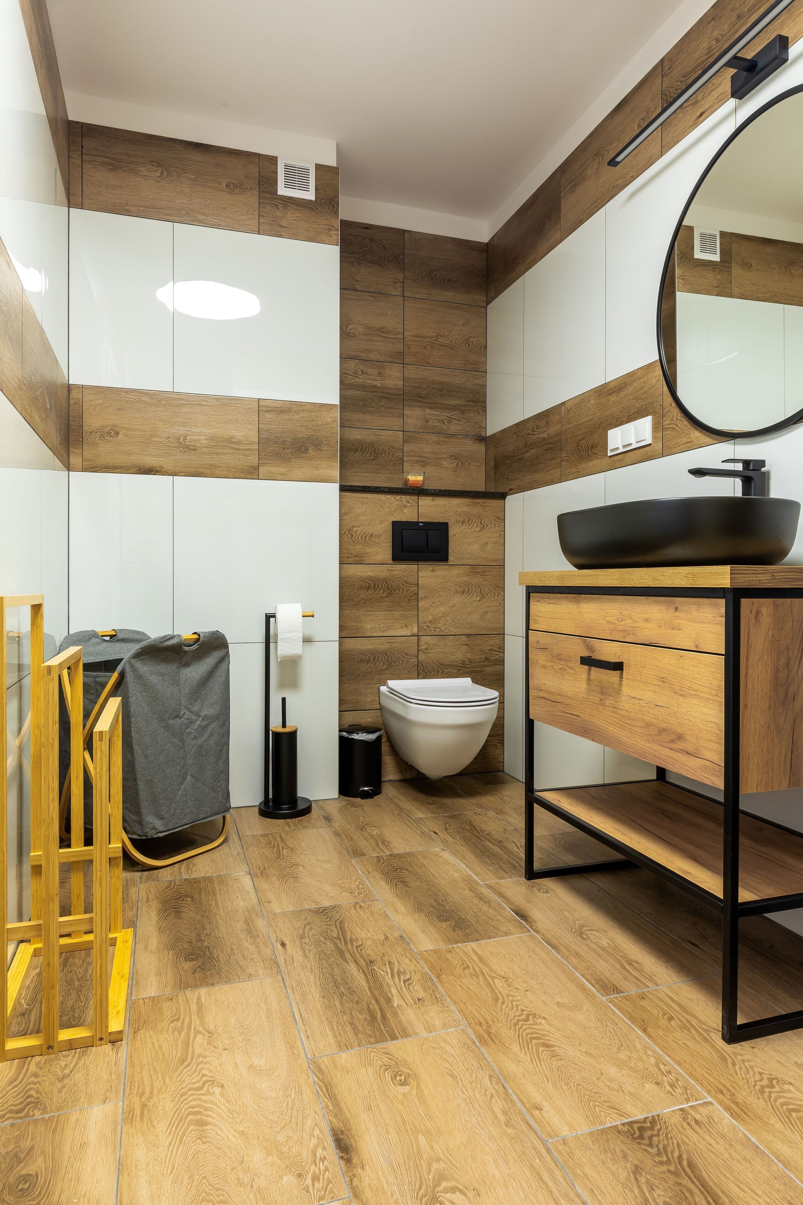 A modern bathroom with wooden flooring, a white toilet, a black sink, and a wooden vanity.