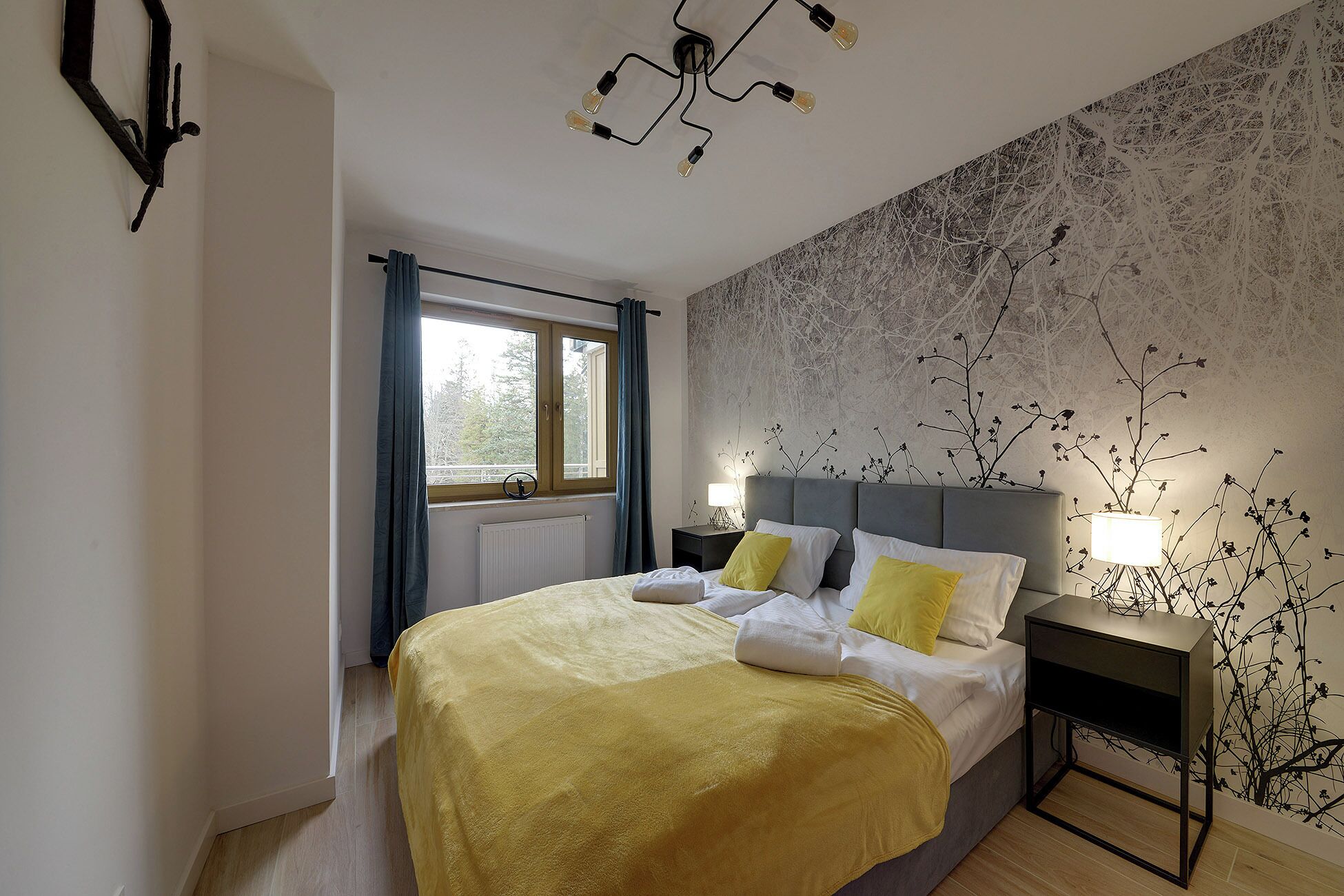 Un dormitorio con cama, mesita de noche, lámpara de pared y ventana con cortinas.