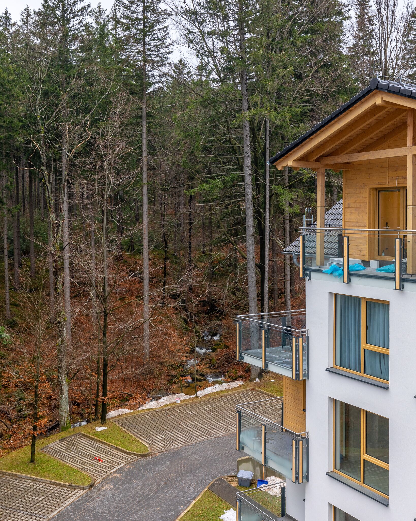 A modern building with a balcony, a wooden deck, and a view of a forested area.