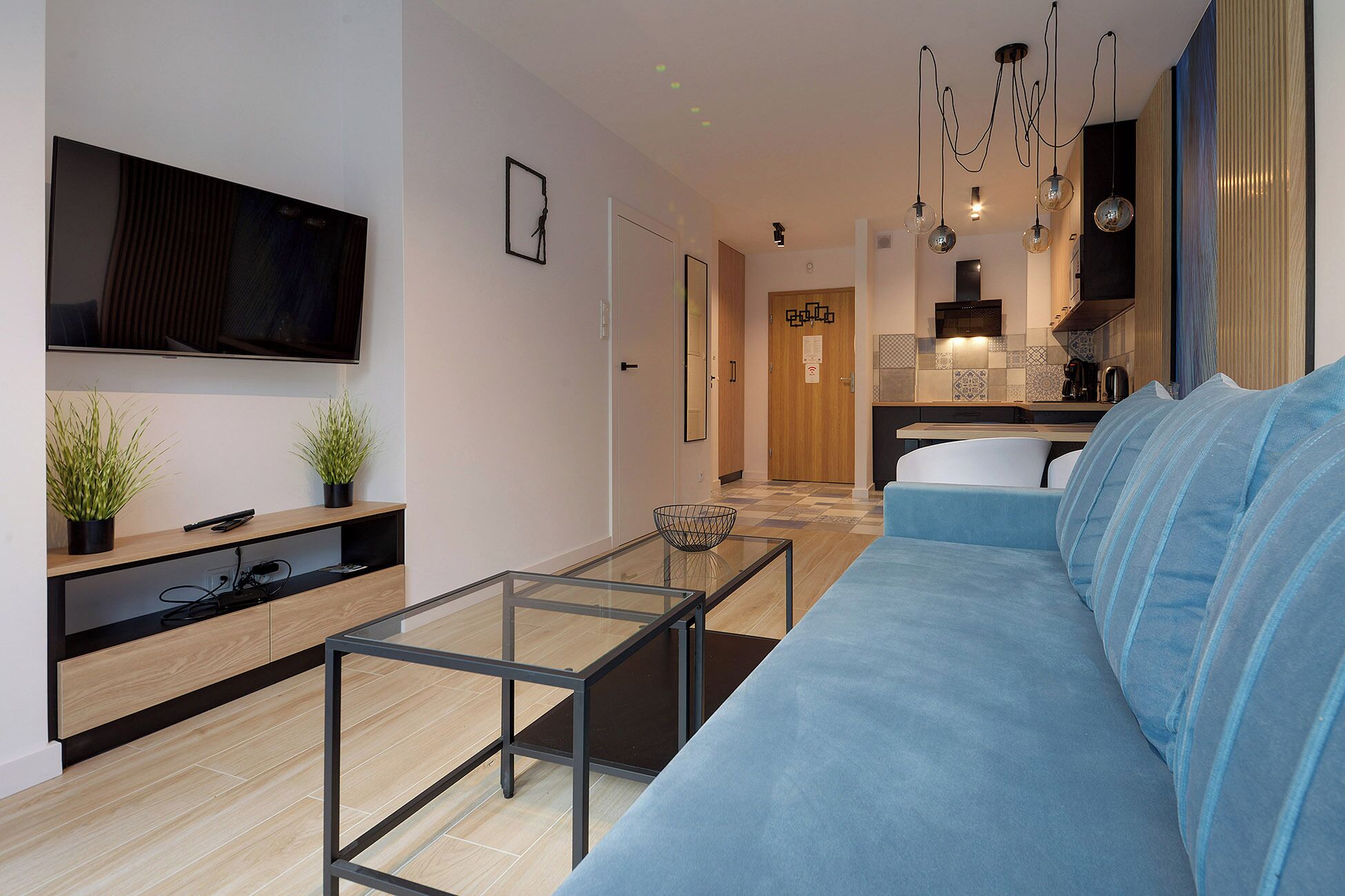 A modern living room with a blue sofa, a glass coffee table, and a flat-screen TV on a wooden shelf.