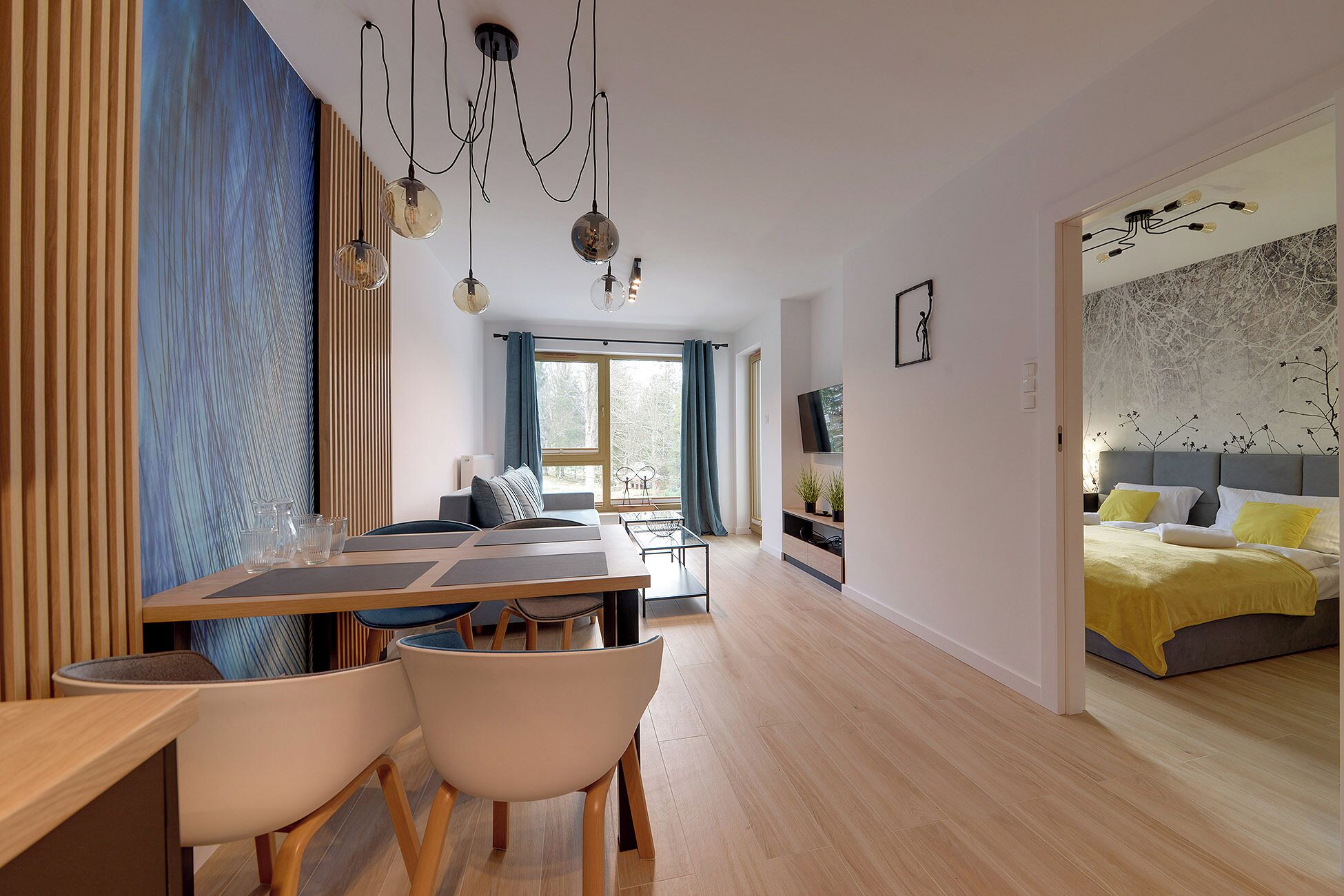 Ein modernes Wohnzimmer mit Essbereich, einem großen Fenster und einem Schlafzimmer mit Bett und Fernseher.