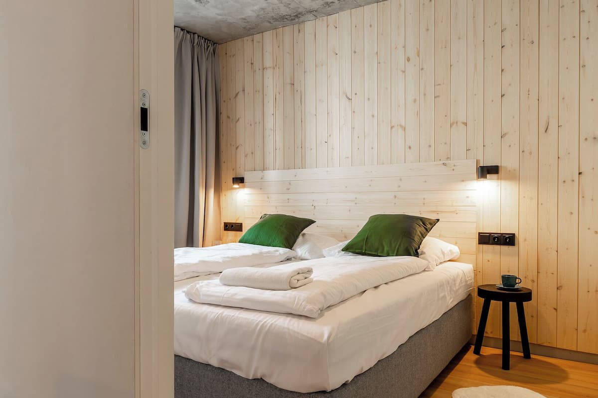 Un dormitorio con cama, dos mesitas de noche, una mesita auxiliar, una alfombra de piel blanca, paredes de madera y techo de hormigón.