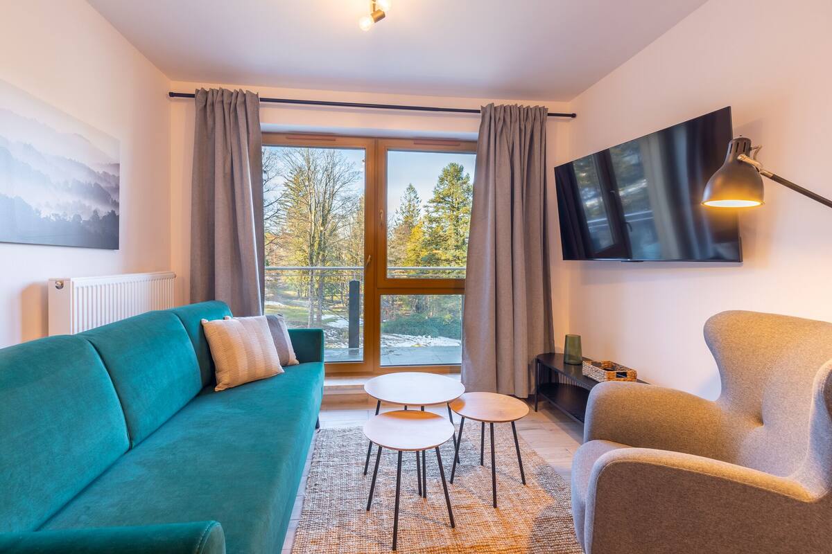 Una sala de estar moderna con un sofá azul turquesa, un sillón beige, una pequeña mesa blanca y un televisor montado en la pared.