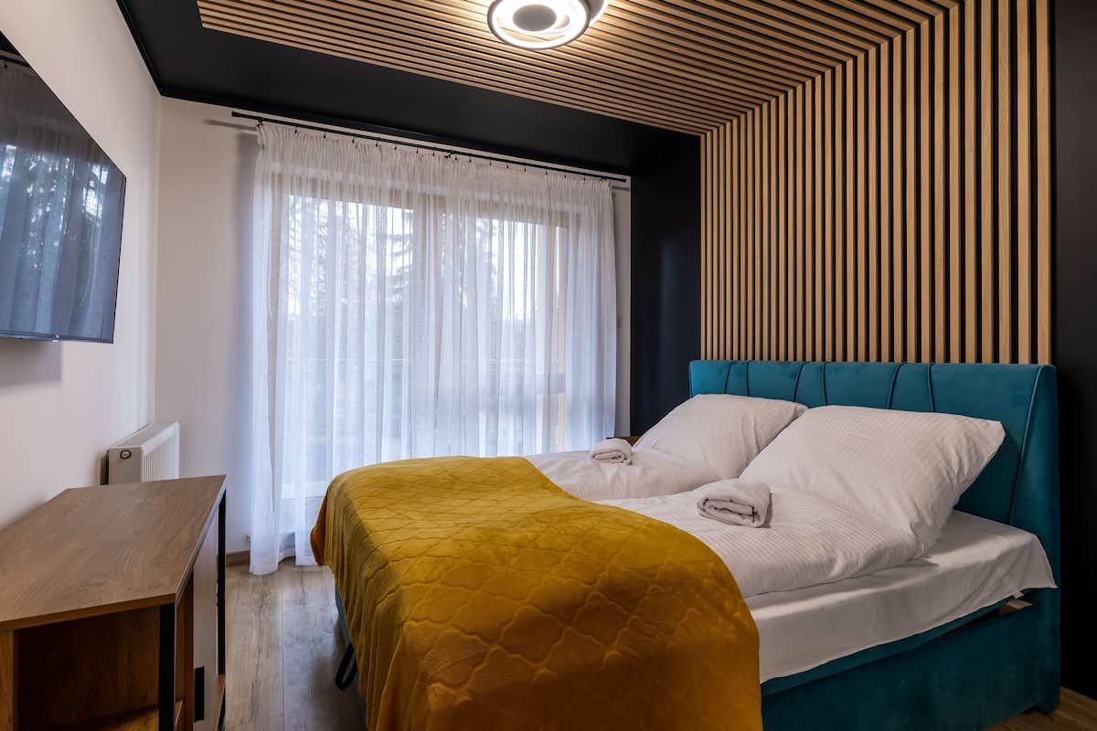Un dormitorio moderno con cama, escritorio y un gran ventanal con cortinas traslúcidas.