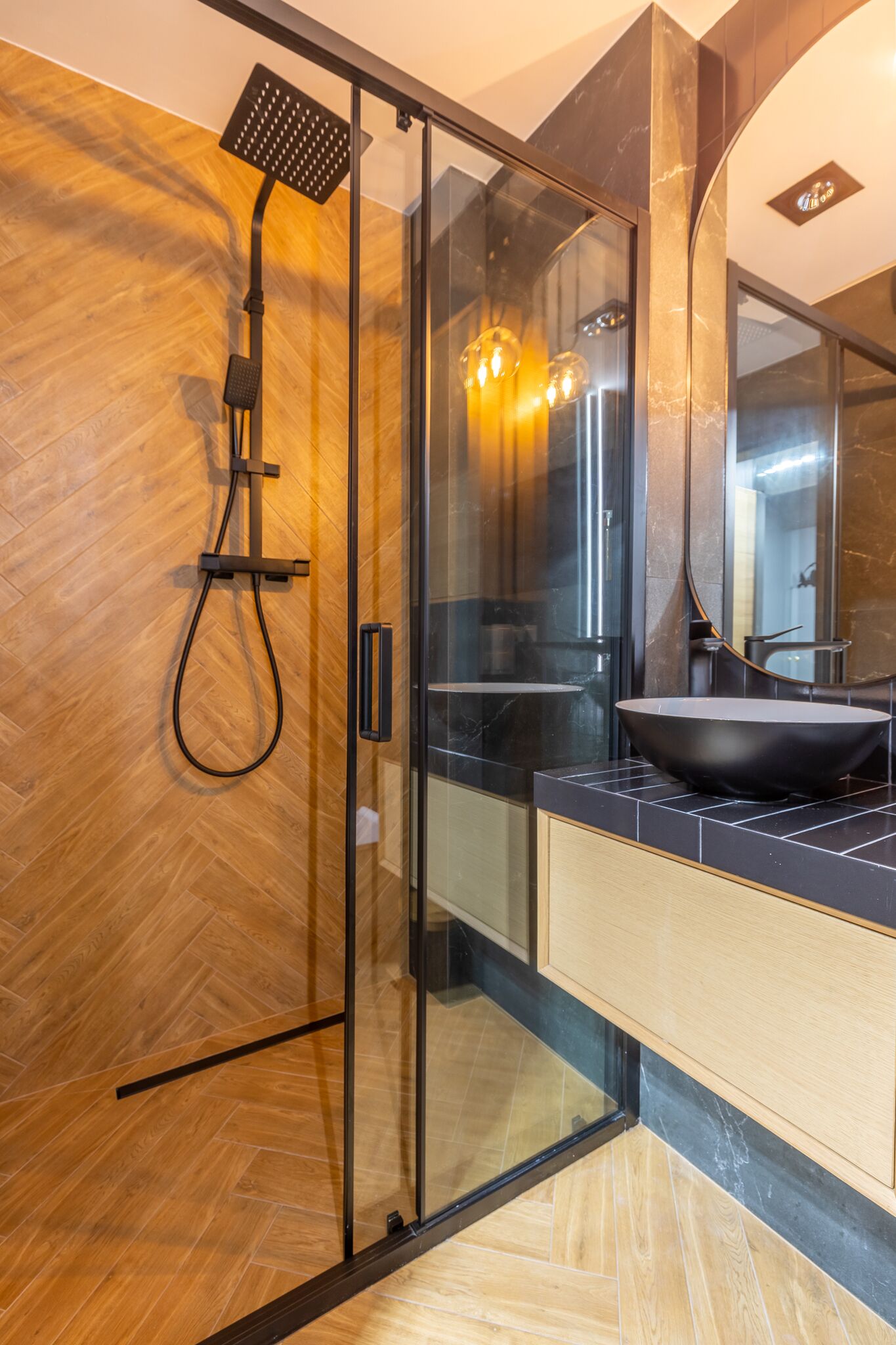 A modern bathroom with a glass-enclosed shower, a black sink, and a wooden floor.