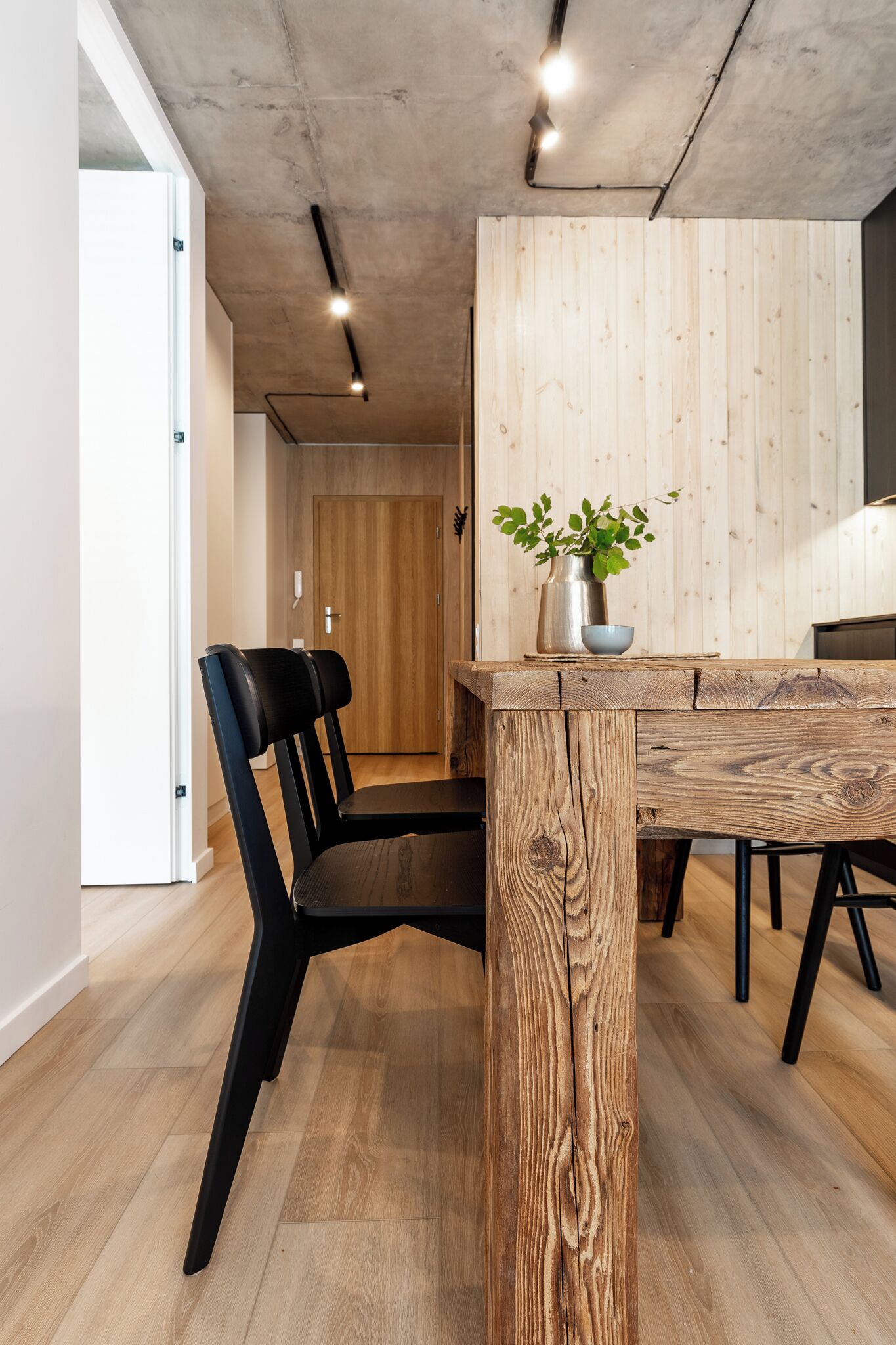 A modern dining area with a wooden table, black chairs, and a potted plant.