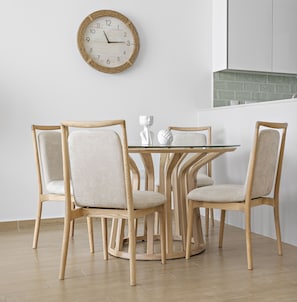 A dining area with a round wooden table, four upholstered chairs, and a wall-mounted clock.