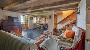 A spacious living area with a wooden ceiling, a dining table, and a sofa with cushions.
