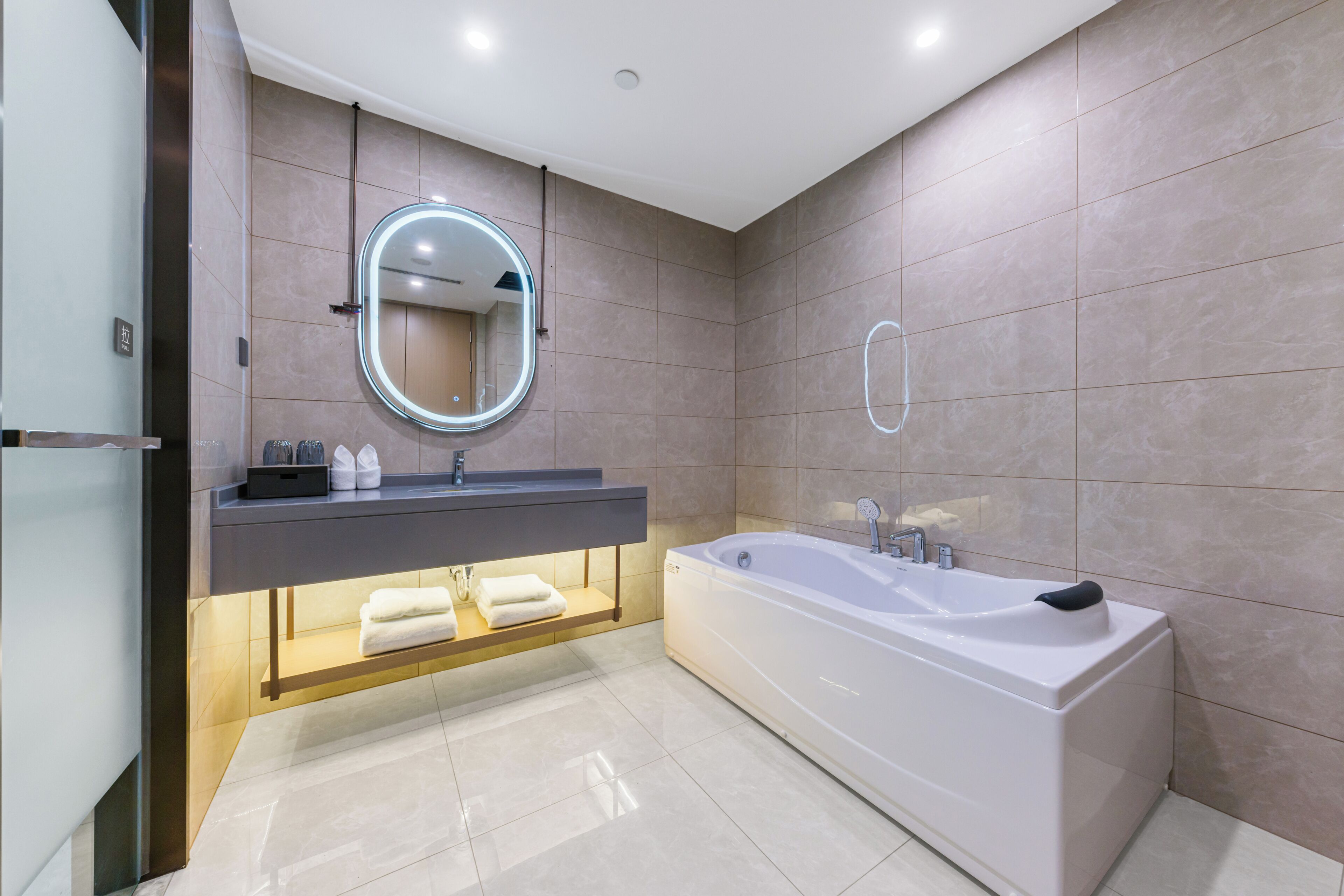 Ein modernes Badezimmer mit einer großzügigen Badewanne, einem runden Spiegel und einem Waschtisch mit Ablagefläche.