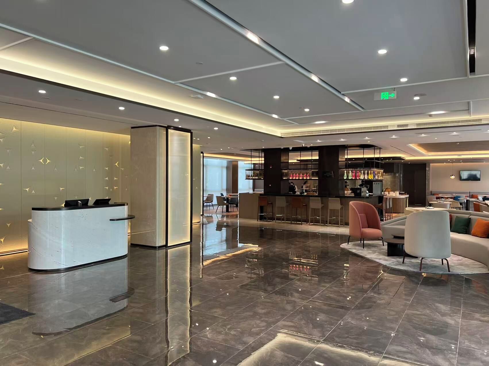 A modern hotel lobby with a reception desk, seating area, and bar.